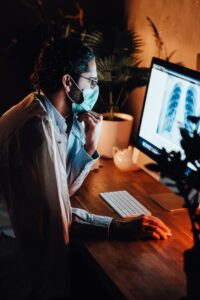 Serious doctor with glasses with computer in dark room